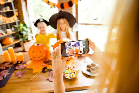 mommy is photographing her kids. Not clear shot of dressed in halloween headwear kids, bonding, mum is taking photo on her telephone, halloween decorations, focus of cellの写真素材