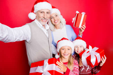 Cheerful siblings and married senior couple take and show gifts with ribbons, in knitted cute x mas...