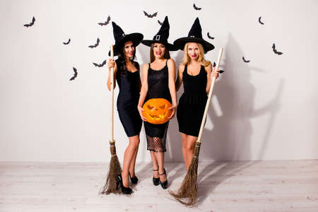 Full length of three terrifyng mysterious mistress monsters in elegant clothing, with bright red lips, long wizard headwears, standing posing on white wall background, with pumpkin cutted head, spookyの写真素材