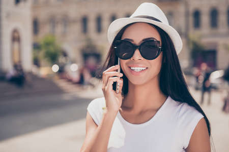 Attractive stylish mixed-race lady with bronze skin and trendy eyewear is speaking on her digital...