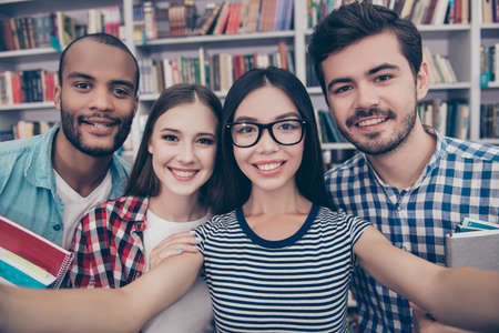 Four students with beaming smiles are posing for selfie shot, asian attractive lady is taking, in...