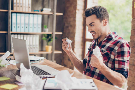Side profile shot of frustrated young brunet entrepreneur,  yelling at his laptop in office and...