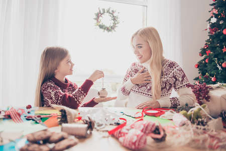 Desktop full of handcraft activity supplies, small lovely blonde haired kid presents her mum a diy, ready for x mas noel, sunshine in window, happiness, upbringing, motherhood conceptの写真素材