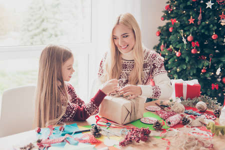 Happiness, upbringing, leisure, friendship, childhood, hobby, x mas, noel concept. Little, lovely blonde with her mom are doing handcraft activity enjoying using rope, ribbon, tape, firtree nearの写真素材