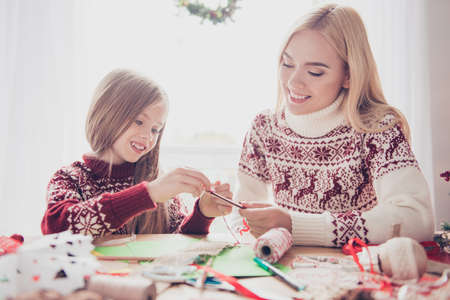 Lovely blonde with her mommy doing handcraft activity, enjoying. Happiness, upbringing, childhood, friendship, leisure, traditions x mas, noel concept, desktop full of materialsの写真素材