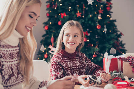 Cute little blonde is so cheerful, watching lovely and sweet at her mommy, they are doing handcraft...