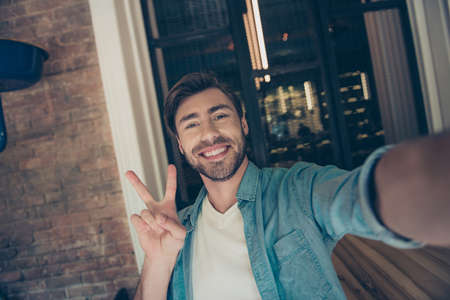 Attractive traveller is doing photoshot for his blog, carefree, wearing denim shirt, with wide...