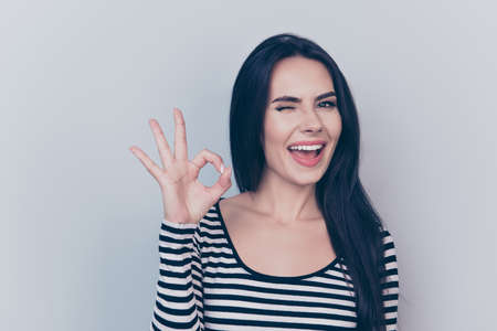 i like it close up portrait of young  dreamy, gorgeous, charming lady, on light grey background, in striped fashionable trendy wear, with long silky dark hair, smooth clean skin, with ok symbolの写真素材