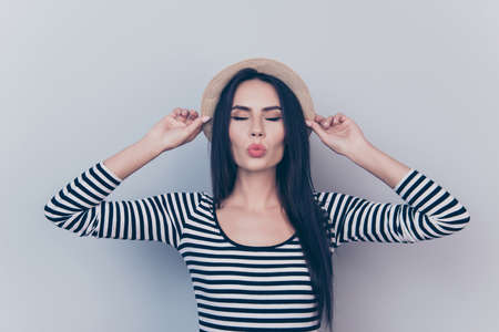 Close up portrait of young charming girlfriend, holding her beige head wear, on grey background, in...
