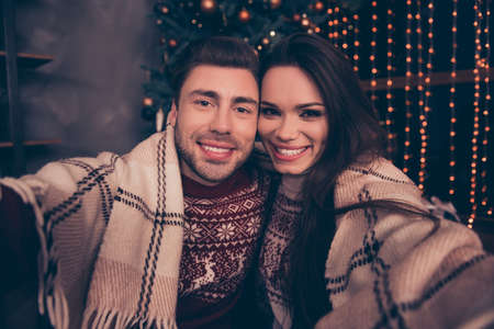 Cheerful caucasian brunet husband and charming pretty brunette wife are doing their portrait. Bonding, hug and embrace, covered to keep warm and cozy, decorated home on backgroundの写真素材