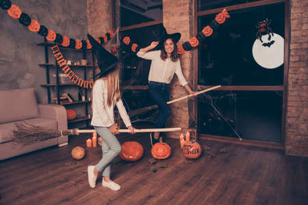 Full-length of mysterious playful, mystical gorgeous fairy enchantresses, mom and small blondie, prepared to take off on broom stick, burning candles, bats, 
childhood, friendship, happinessの写真素材