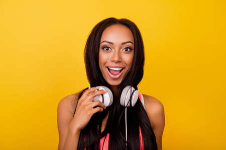 Very cheerful emotional dreamy stylish afro lady with bronze skin, long dark hairstyle, so hot, enjoying to the stereo sound in big modern ear phones on her neck, singing, yelling, shouting, pop eyedの写真素材