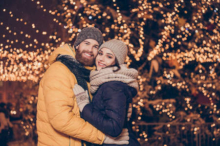 Portrait of cute family hugging each other and smiling while having a stroll at x mas evening in the town, in warm outfits, headwear, many sparkling decorations on the backgroundの写真素材