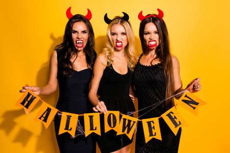 Welcome to night feast of death! Spooky horned zombies bonding, holding the paper bunting flags garland in spider nets, isolated on background, in nice hot outfits, hissing, inviting you to celebrateの写真素材