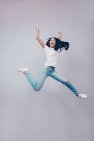 Success, dream, femenine girlish life concept. Chill relaxing mode. Excited mixed race brunette lady model is jumping up, wearing casual clothes, white shoes, on pure light grey background,の写真素材