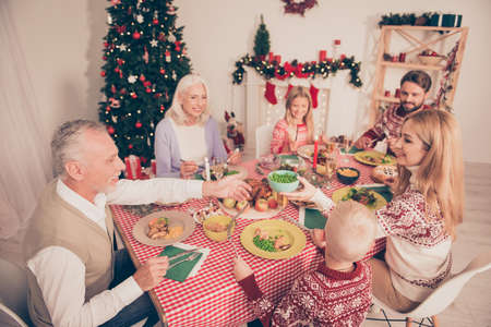 Six cheerful relatives, setted festive desktop, full of yummy treats, married couples, siblings, grandad, granny, in knitted traditional x mas costumes, pine firtree, decorated room, bon appetite!の写真素材