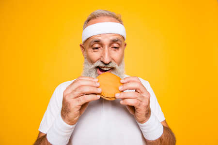 Close up of modern athlete cool grey haired pensioner grandpa hold yummy tasty delicious heavy grossy sandwich, destroys it. Weightloss, healthcare, gym, strength, regime, challenge lifestyleの写真素材