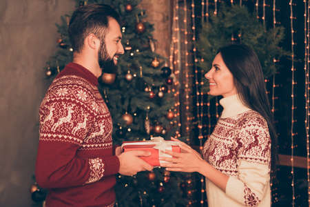 Sweet husband and wife are receiving gifts with white ribbon, at home indoors, so excited, in...