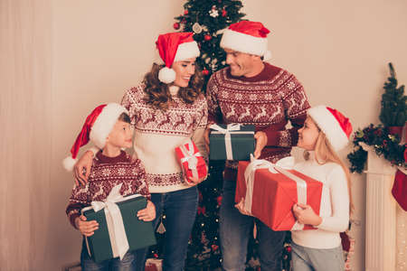 Four cute relatives at home, married couple, parents, mom and dad, excited siblings, in knitted cute traditional x mas costumes, so excited about x mas noel gifts, wrapped with bows tape ribbonsの写真素材