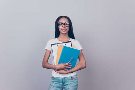 Cute afro with is standing on pure background isolated, in casual outfit, denim jeans, black trendy eye wear specs, with colorful note pads, clipboard, looking cheerful in cameraの写真素材