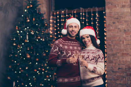 Festive friends with stemware of martini embrace bonding, so excited in knitted cute traditional x mas costumes with ornament, headwear, jeans, enjoy, december time, firtree, garland, nightの写真素材