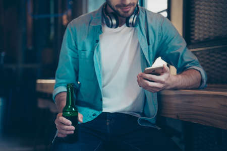 Chilling, technology, enjoying free time. Good life alone. Close up cropped of bearded music lover with bottle at the bar, sitting in casual smart, trendy and fashionable, watching at his telephoneの写真素材