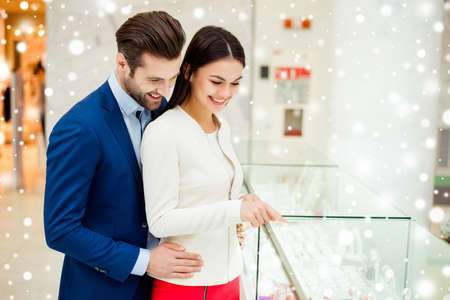 Happy successful stylish lovely couple together make shopping near showcase. Young elegant girlfriend pointing at glass case with ring and
earring for her boyfriend, winter xmas snowflakes backgroundの写真素材