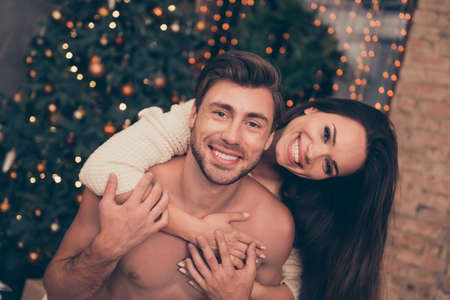 True feelings! Close up of adorable, lovely, sensual cute friends cuddling, brunette lady is with beaming smile, cute guy, so cheerful, at home, pine fir tree, sparkles, winter, happinessの写真素材
