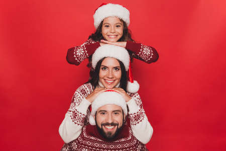 Close up of three cheerful beautiful relatives, married couple, excited girl with mom and dad, in knitted cute traditional x mas costumes, arms on each others headの写真素材