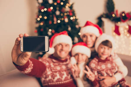 Not clear view of four bonding relatives, at home, married couple, parents, mom and dad, siblings show v sign peace two fingers gesture, in knitted cute traditional x mas costumes, friendship, loveの写真素材