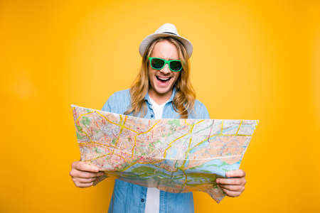 Oh no! Portrair of young shocked man looking in open road map on yellow background. A tourist on summer vacation. Adventures seekerの写真素材