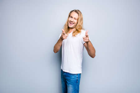 I choose you! Portrait of charming happy young guy dressed in casual clothes, he is giving a wink and indicating with his fingers, isolated on grey backgroundの写真素材