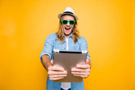 Portrait of angry tourist in summer glasses screaming with open mouth while watching something on laptop standing over yellow backgroundの写真素材