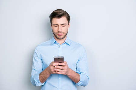 Close up portrait of serious successful manager with bristle looking at his telephone and typing sms through 5g internet while standing over grey backgroundの写真素材
