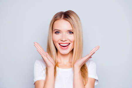Concept of perfect clean skin and ideal teeth. Close up portrait of happy joyful carefree woman with blonde hair who is holding the hands near her face. She is isolated on grey backgroundの写真素材
