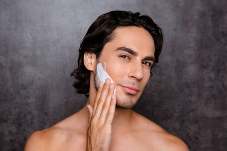Close up of face of cheerful mulatto hispanic man with white foam on his face, isolated on grey background, so hot, nude chest, black nice hair, clean skin, applies the creamの写真素材