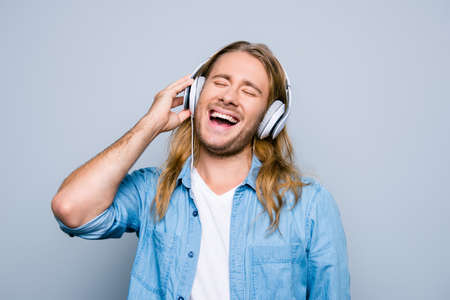 Close up portrait of caucasion bristle guy listening his favorite music, singing the song, holding  earphones on the head standing over grey backgroundの写真素材