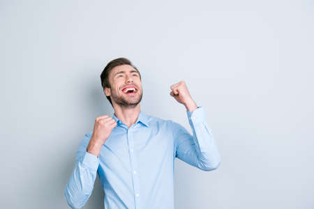 Shot of  overjoyed, successful young manager looking up with his arms raised and celebrating victory while standing in front of grey backgroundの写真素材