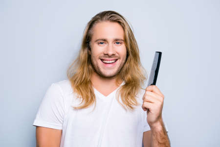 Concept of finding treatment against dandruff using correct shampoo and conditioner for men, close up portrait of happy joyful young guy demonstrating a comb in his hand, dressed in casual clothesの写真素材