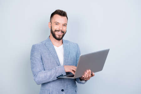 Close up portrait of cheerful brunet bearded business man in formal wear, typing on his laptop, he is a successful lawyer, standing browsing on his device, blue backgroundの写真素材