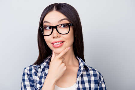 Attractive pretty girl in casual clothing and spectacles is thinking about new steps in career ladder, she is isolated on grey backgroundの写真素材