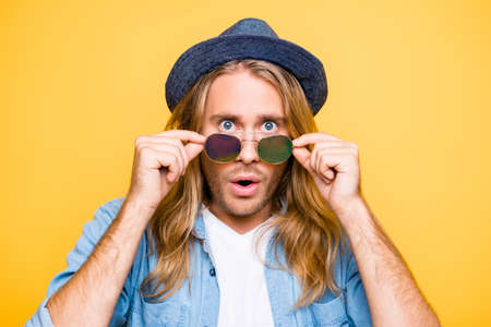 Really? Close up portrait of shocked bearded blond attractive guy holding glasses with fingers, amazed with open mouth, looking over glasses, standing over yellow backgroundの写真素材
