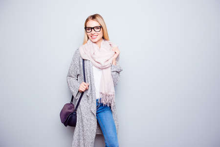 Portrait of attractive happy careless young woman with beaming smile is wearing warm cardigan, scarf and holding her purple handbag. She is isolated on grey backgroundの写真素材
