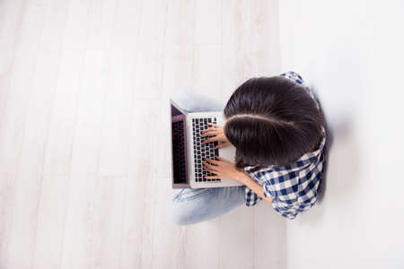 Top view photo of experienced journalist in casual clothes with a laptop on her crossed legs is typing an article for a fashion magazineの写真素材