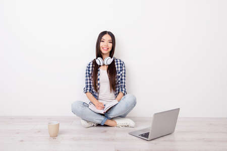 Pretty cute young female student is doing her homework, listening to music and preparing for the exams. She uses a computer and drinking coffeeの写真素材