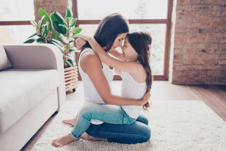 Domestic atmosphere! Careful mother is showing her support! Happy mother and daughter are sitting on the floor and hugging with closed eyesの写真素材