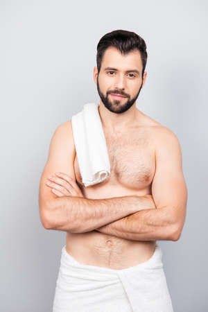 Portrait of narcissistic, caucasian man with naked torso, folded hands, having towel on his shoulder, looking at camera, standing over grey backgroundの写真素材