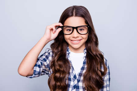 Closeup portrait of smart attractive little girl in checkered shirt  holding her spectacles  smiling looking to the camera standing over grey backgroundの写真素材