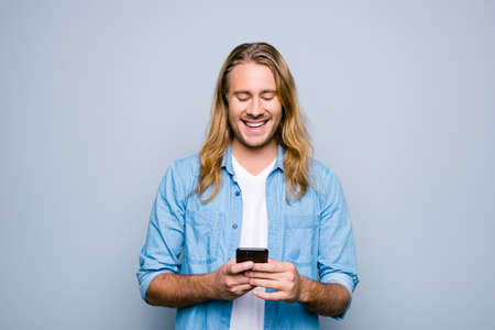 Stylish happy smiling young guy wearing casual clothes is having a chat using his telephone, isolated on grey backgroundの写真素材