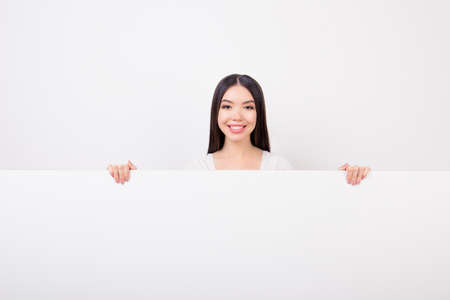 Copy space portrait of charming, attractive, cute girl hiding, standing behind empty white horizontal wall isolated over white backgroundの写真素材